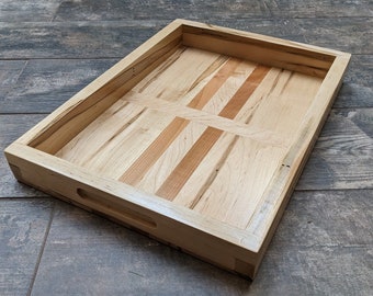 May include: A rectangular wooden tray with a natural wood finish. The tray has a raised edge and a handle on one side. The tray is made of maple wood with a unique grain pattern.
