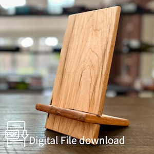 Pode incluir: Um suporte de telefone de madeira com acabamento em madeira natural. O suporte é feito de madeira de cerejeira e tem um design simples. O suporte é perfeito para segurar um telefone no modo retrato ou paisagem. Download de arquivo digital.