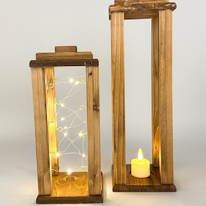 May include: Two wooden candle lanterns, one with a string of fairy lights and the other with a white pillar candle. Both lanterns have a rustic brown finish.