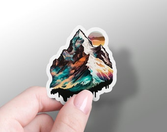 Puede incluir: Una pegatina colorida que presenta una cordillera con una puesta de sol en el fondo. La montaña está pintada en tonos de azul, verde, naranja y marrón. La pegatina tiene un efecto de goteo alrededor de los bordes.