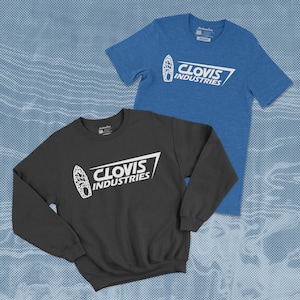 Puede incluir: Dos camisas con un gráfico blanco de una tabla de surf con el texto "Clovis Industries" en una camisa azul y negra.