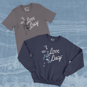 May include: Two shirts with the text "I Love Lucy" printed on them. One shirt is a grey t-shirt and the other is a navy blue sweatshirt.