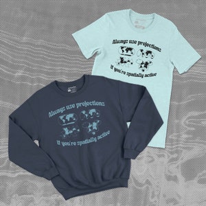 May include: Two shirts with the same graphic design. A navy blue sweatshirt and a light blue t-shirt both feature the text "Always use projections if you're spatially active" with a graphic of four different map projections.