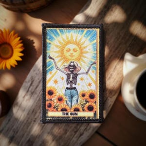 May include: A rectangular patch with a black border features a tarot card design. The card depicts a skeleton figure with arms raised, standing in front of a smiling sun and sunflowers. The text "THE SUN" is at the bottom.
