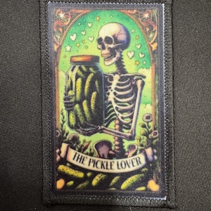 May include: A rectangular patch featuring a skeleton holding a jar of pickles. The skeleton is in a colorful, whimsical setting with hearts and flowers. The text "THE PICKLE LOVER" is displayed on a banner below the image.
