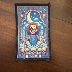 May include: Rectangular patch with a colorful illustration of a doll with red hair and blue overalls, surrounded by skulls, candles, and a crescent moon. The text "THE KILLER" is at the bottom. The patch has a black border.