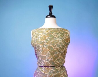 May include: A vintage two-piece dress on a mannequin. The sleeveless top and matching skirt feature a cream-colored paisley pattern with green and orange accents. The dress is displayed against a blue background.