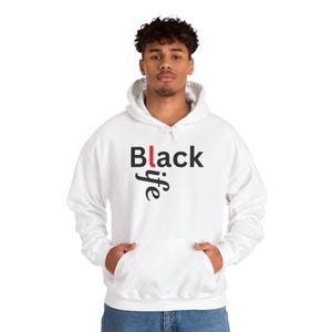 May include: White hoodie featuring the text "Black life" in black and red. The word "life" is written in a stylized font. The sweatshirt has a front pocket and a drawstring hood.