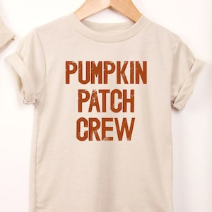 May include: A beige t-shirt with the text "Pumpkin Patch Crew" in orange.