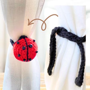Crochet ladybug curtain tieback shown wrapped around a white curtain, with a red and black spotted ladybug on one side and black crochet ties on the other.