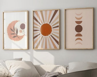 May include: Three framed prints with abstract designs in shades of brown, orange, and pink. The prints depict a crescent moon with a branch, a sun with rays, and a series of crescent moons.