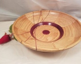 Op de afbeelding: Een grote houten kom met een natuurlijke houtkleur en een diep rood centrum. De kom heeft een uniek ontwerp met een spiraalvormig patroon en een verhoogde rand.