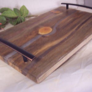 May include: A wooden serving tray with a natural wood finish and a clear epoxy resin inlay. The tray has two black metal handles.