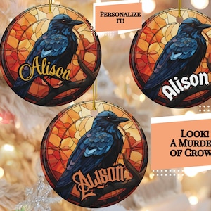 May include: Three round, personalized Christmas ornaments featuring a stained glass design of a blue crow perched on a branch. The ornaments are decorated with a warm orange, yellow, and red background. The name "Alison" is written in gold lettering on each ornament.
