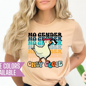 May include: A beige t-shirt with a retro-style graphic of a goose wearing a hat and holding a flag. The text "No Gender, Only Goose" is printed on the shirt.