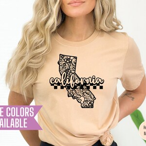 Peut inclure: Un t-shirt beige avec un contour noir de l'état de Californie avec le mot "california" écrit en noir. Le contour de l'état est rempli d'un motif floral noir.