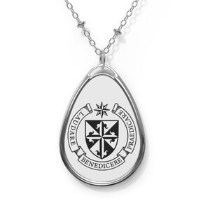 May include: A silver necklace with a teardrop-shaped pendant featuring a black and white crest with the words "LAUDARE", "PRAEDICARE", and "BENEDICERE" around it.