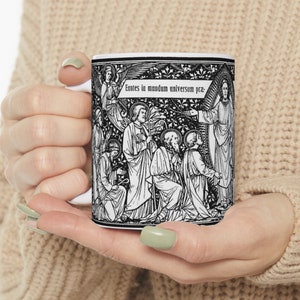 May include: A white ceramic mug featuring a black and white illustration of a religious scene. The illustration shows a group of people gathered around a figure with outstretched arms. The text "Euntes in mundum universum pra." is printed on the mug.