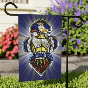 以下が含まれることがあります： 青い背景に白い子羊が雲の上に立っているステンドグラス風のガーデンフラッグ。子羊は金色の後光と十字架で囲まれています。フラッグは黒い金属製のガーデンフラッグスタンドに取り付けられています。