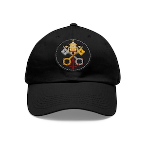 Peut inclure: Casquette de baseball noire avec un patch circulaire représentant des clés papales et une tiare dorées et argentées.