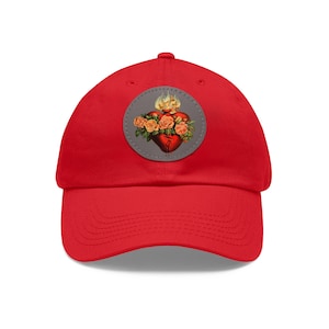 Peut inclure: Casquette de baseball rouge avec un patch gris représentant une image stylisée d'un cœur avec des flammes et des roses.