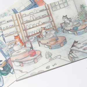 May include: A watercolor illustration of a pottery studio with four cats working on pottery. One cat is using a pottery wheel, another is shaping clay on a table, and two are working on pottery wheels. The studio has shelves filled with pottery and a potted plant.