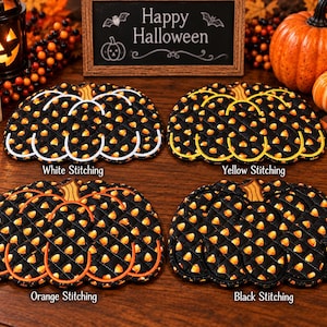 May include: Four quilted pumpkin-shaped hot pads featuring a black fabric with a yellow and orange candy corn pattern. Each hot pad has distinct decorative stitching in white, yellow, orange, or black thread outlining the pumpkin shape.
