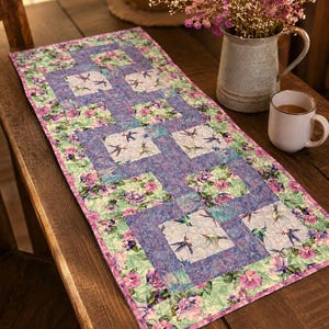 May include: A rectangular fabric table runner featuring a patchwork design with alternating squares of hummingbird illustrations on a light background and purple floral patterns, bordered by a vibrant green and pink floral print fabric.