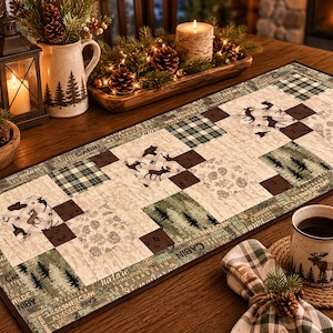 May include: A rectangular fabric table runner featuring a patchwork design with alternating squares of forest-themed prints, including moose, pine trees, plaid patterns, and pinecones, bordered by text reading nature, cabin, and wilderness.