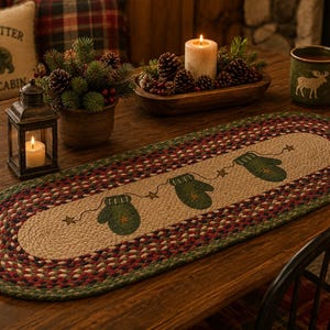 May include: An oval braided table runner featuring a tan center with a repeating pattern of three green mittens connected by a thin line with small stars. The border consists of concentric braided rings in shades of green, red, and dark brown.