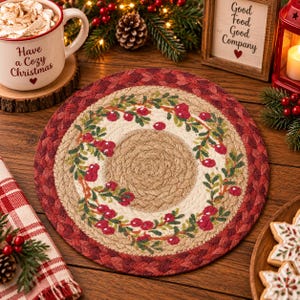 May include: A round braided table mat featuring a central tan circle surrounded by a cream-colored ring decorated with a pattern of green holly leaves and red berries, finished with a wide outer border of deep red braided material.