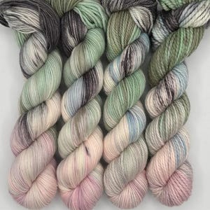 May include: Four skeins of yarn in shades of green, pink, and gray. The yarn is twisted into a spiral shape.