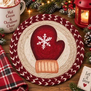 May include: A round, braided fabric mat featuring a central design of a red mitten with a white snowflake pattern and a tan cuff. The mat has a beige inner circle surrounded by a thick, dark red braided border with a white chevron pattern.