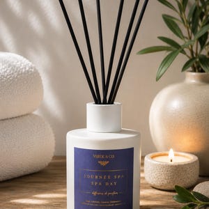 May include: A white cylindrical reed diffuser bottle with six black reeds. The label is dark blue with gold text reading VERDE & CO, JOURNÉE SPA, SPA DAY, diffuseur de parfum, Sage, Lavande, Davana, Cedarwood, 5 OZ | 150 ML.