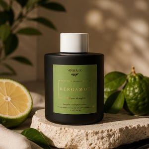 May include: A matte black cylindrical reed diffuser bottle with a white cap and a green label. The label features the text VERDE & CO, BERGAMOT, and 5 OZ | 150 ML. The bottle is positioned next to a sliced green citrus fruit and black diffuser reeds.