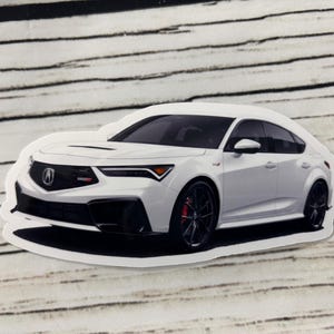 May include: White car sticker featuring a modern sedan with black accents and red brake calipers. The car has a sleek design with a prominent front grille and headlights. The sticker is on a white background with black lines.