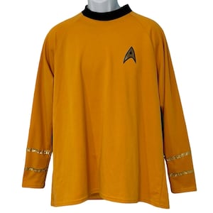 May include: Mustard yellow long-sleeve shirt with a black collar and gold accents on the sleeves. Features a black and gold Starfleet insignia on the chest. A costume-themed garment.