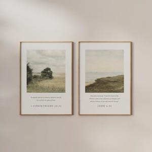 May include: Two framed landscape prints with gold frames. One print depicts a field with a tree, the other a coastal scene. Each print has a Bible verse at the bottom. The first print has the text "1 CORINTHIANS 10:31". The second print has the text "JOHN 6:35".