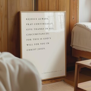 May include: A rectangular framed wall art piece featuring a light cream background with black serif text that reads: REJOICE ALWAYS, PRAY CONTINUALLY, GIVE THANKS IN ALL CIRCUMSTANCES; FOR THIS IS GOD'S WILL FOR YOU IN CHRIST JESUS. 1 THESSALONIANS 5:18.