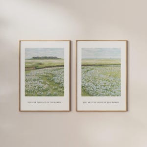 Könnte beinhalten: Zwei gerahmte Landschaftsdrucke. Jeder zeigt ein Feld weißer Blumen, grünes Gras und eine entfernte Baumreihe unter einem bewölkten Himmel. Der Text am unteren Rand des linken Drucks lautet: „YOU ARE THE SALT OF THE EARTH“. Der rechte Druck lautet: „YOU ARE THE LIGHT OF THE WORLD“.