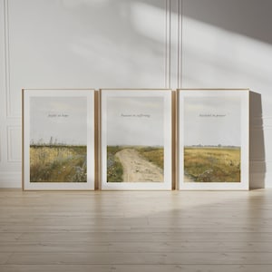 Könnte beinhalten: Drei gerahmte Landschaftsdrucke mit inspirierenden Zitaten. Die Drucke zeigen eine gedämpfte Farbpalette aus Beige, Gelb und Grün, die Felder und eine unbefestigte Straße darstellen. Die Zitate lauten: „Freudig in der Hoffnung“, „Geduldig im Leid“ und „Treu im Gebet“.