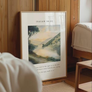 Pode incluir: Um quadro retangular emoldurado com uma pintura de paisagem de um lago calmo rodeado por colinas ao pôr do sol. O texto ISAIAH 30:21 aparece no topo e o versículo está impresso na parte inferior com uma fonte serifada preta.