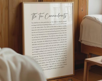 May include: A framed wall art print featuring the text of The Ten Commandments in a black serif font on a cream background. The title is written in a black cursive script at the top. The print is enclosed in a thin, light-colored wooden frame.