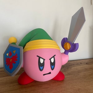 May include: A pink and red 3D printed figurine of a character from the video game Kirby, holding a sword and shield. The character is wearing a green hat with a yellow band.
