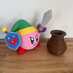 May include: A pink and red character with a green hat and a sword, holding a blue and red shield with a red bird design. The character is standing on a wooden surface next to a brown clay pot.