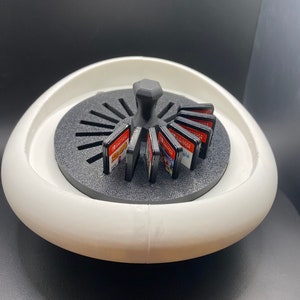 May include: White rotating carousel game cartridge holder with a black center knob and black game cartridges. The holder is designed to hold Nintendo Switch game cartridges.