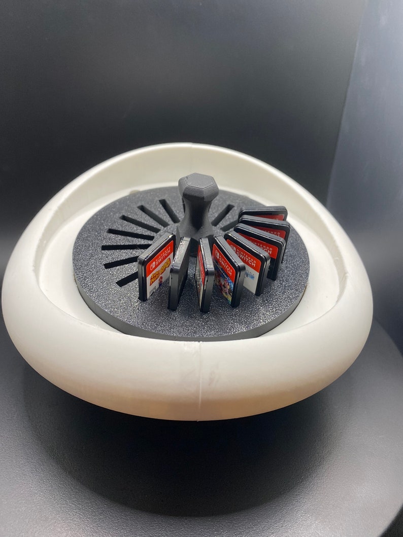 May include: White rotating carousel game cartridge holder with a black center knob and black game cartridges. The holder is designed to hold Nintendo Switch game cartridges.