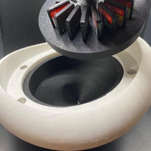 May include: A white, 3D printed, egg-shaped container with a black, rotating lid. The lid holds multiple Nintendo Switch game cartridges.
