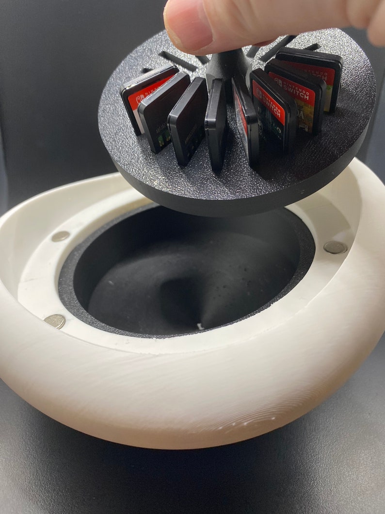 May include: A white, 3D printed, egg-shaped container with a black, rotating lid. The lid holds multiple Nintendo Switch game cartridges.