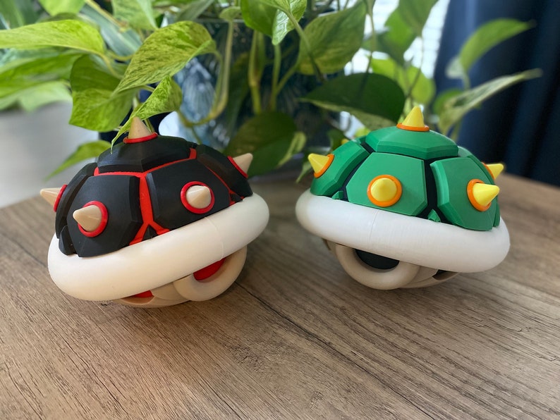 May include: Two 3D printed Super Mario Bros. Koopa Troopa shells. One is black with red accents and the other is green with yellow accents.